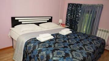 Una cama individual con cabecera, una mesita de noche con lámpara y una ventana con cortinas.