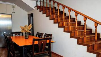 A dining area with a wooden table and chairs, a vase with dried plants, and a wooden staircase.