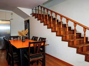 Un comedor con una mesa y sillas de madera, un jarrón con plantas secas, y una escalera de madera.