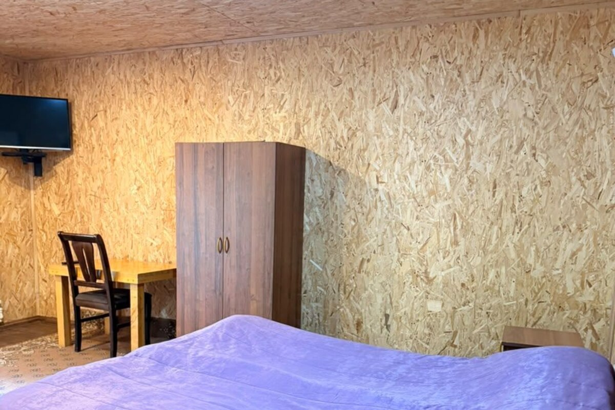 Una habitación con una cama, un armario de madera, un televisor montado en la pared y una silla.