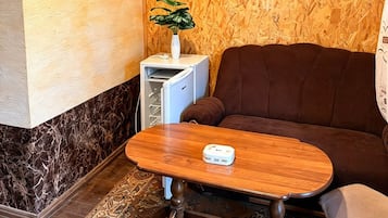 Una habitación con techo de madera, un sofá marrón, una mesita con un florero y una alfombra estampada.