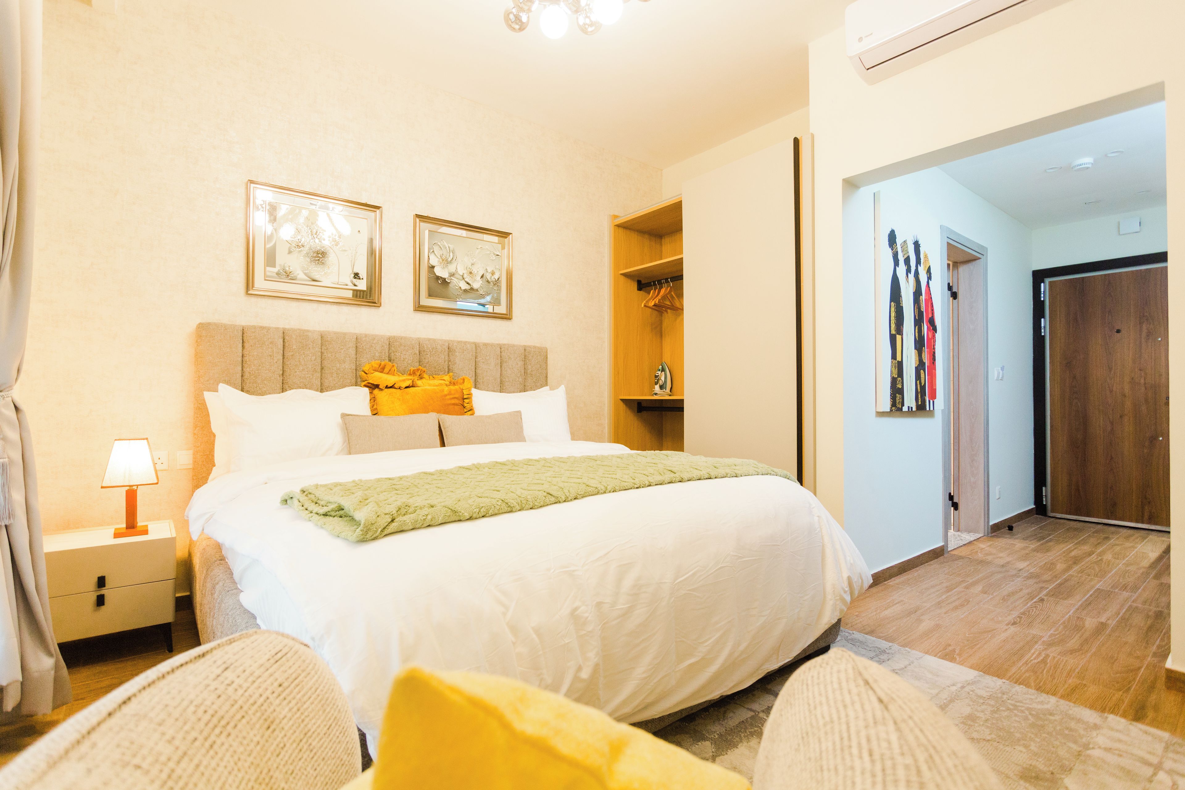 A hotel room with a bed, bedside table, lamp, and two framed artworks on the wall.