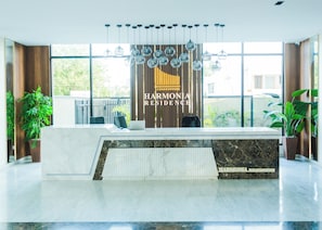 Bancada de recepção com uma placa indicando 'HARMONIA RESIDENCE', um laptop e uma planta sobre a mesa.