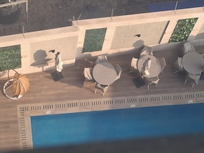 Área de piscina no terraço, com mesas, cadeiras, uma estátua e uma planta ornamental.