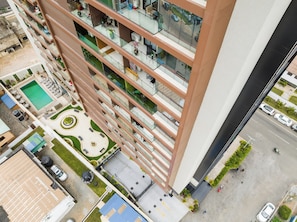 Um edifício alto com várias varandas, piscina no terraço e pátio ajardinado.