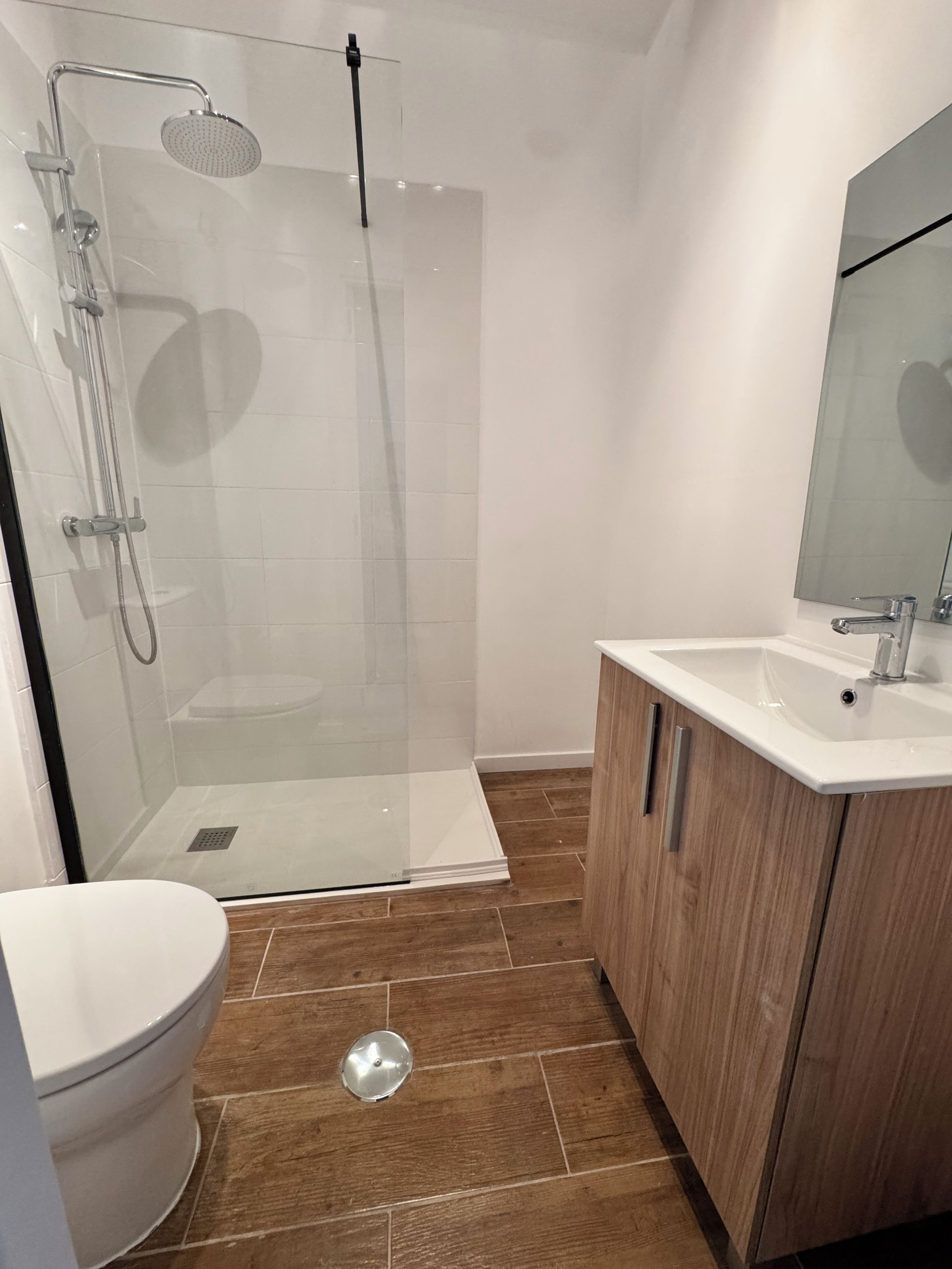 Een moderne badkamer met een douchecabine van glas, een wit toilet en een houten wastafelmeubel met spiegel.