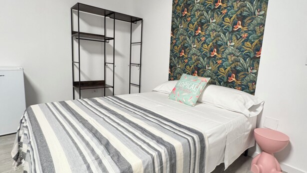 A bedroom with a bed, a wardrobe, a toilet, and a patterned wall. - APARTAMENTOS MELISA 12 (Madrid)