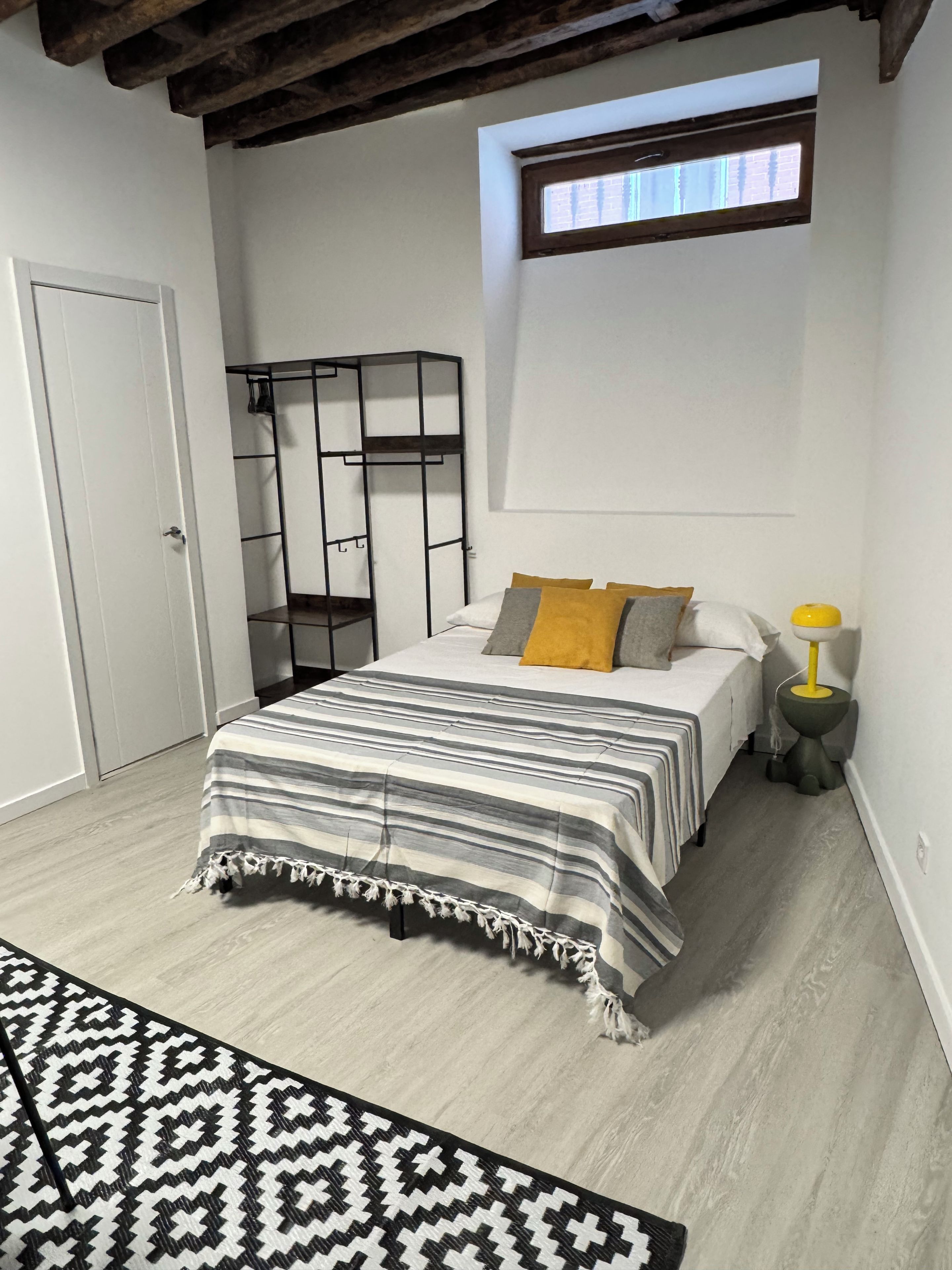 A bedroom with a bed, a window, a wardrobe, and a bedside lamp.