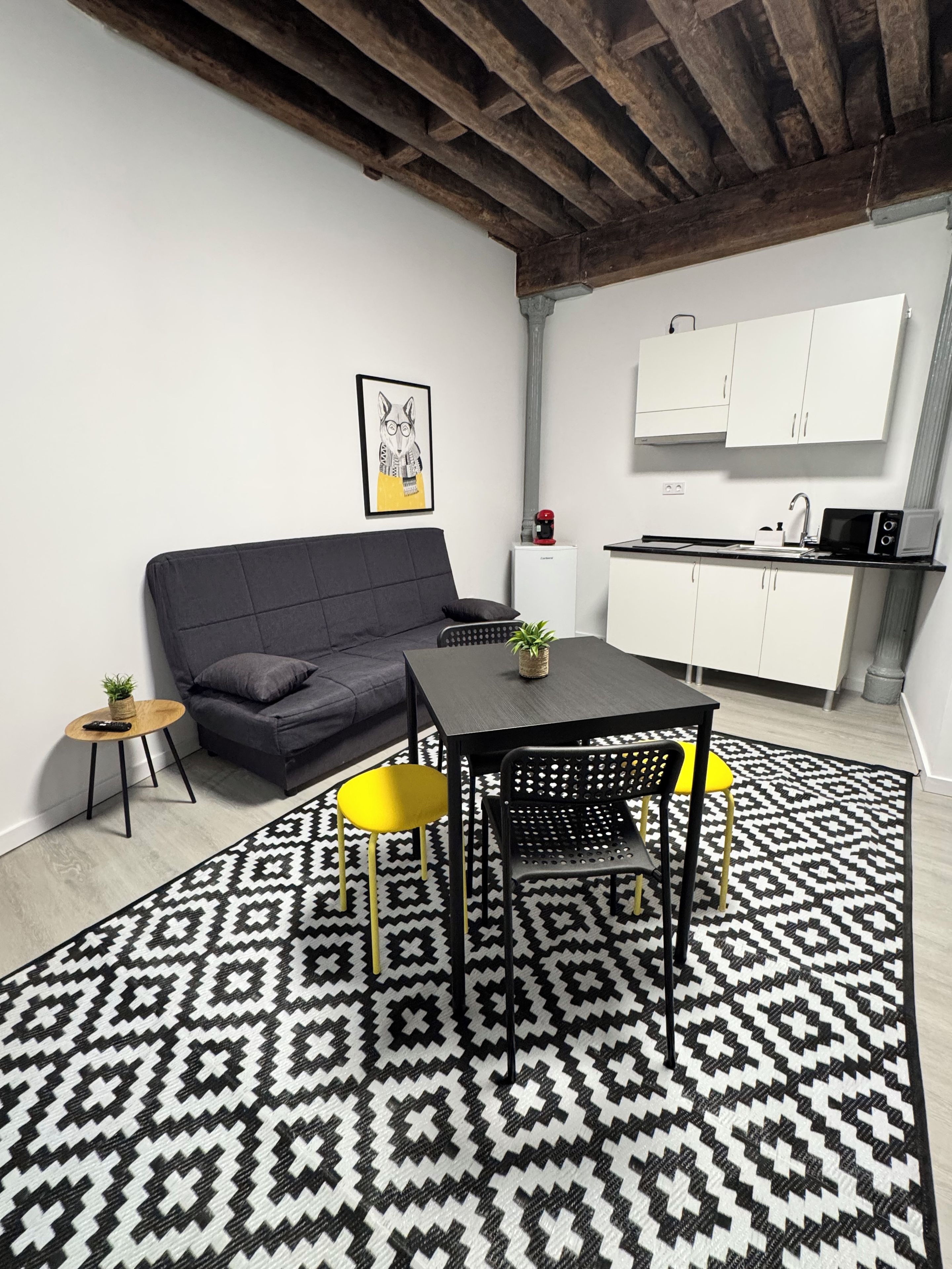 A modern living space with a sofa, a dining table with chairs, a kitchen area, and a patterned rug.