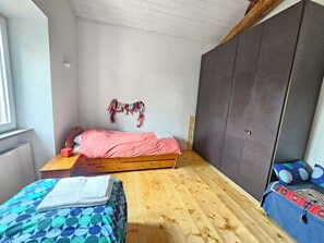 A bedroom with a wooden floor, a bed with a pink bedspread, a wooden nightstand, a wardrobe, and a window. - Villa Paradiso in Sabina: Relaxation, Views, and Nature (Montopoli di Sabina)