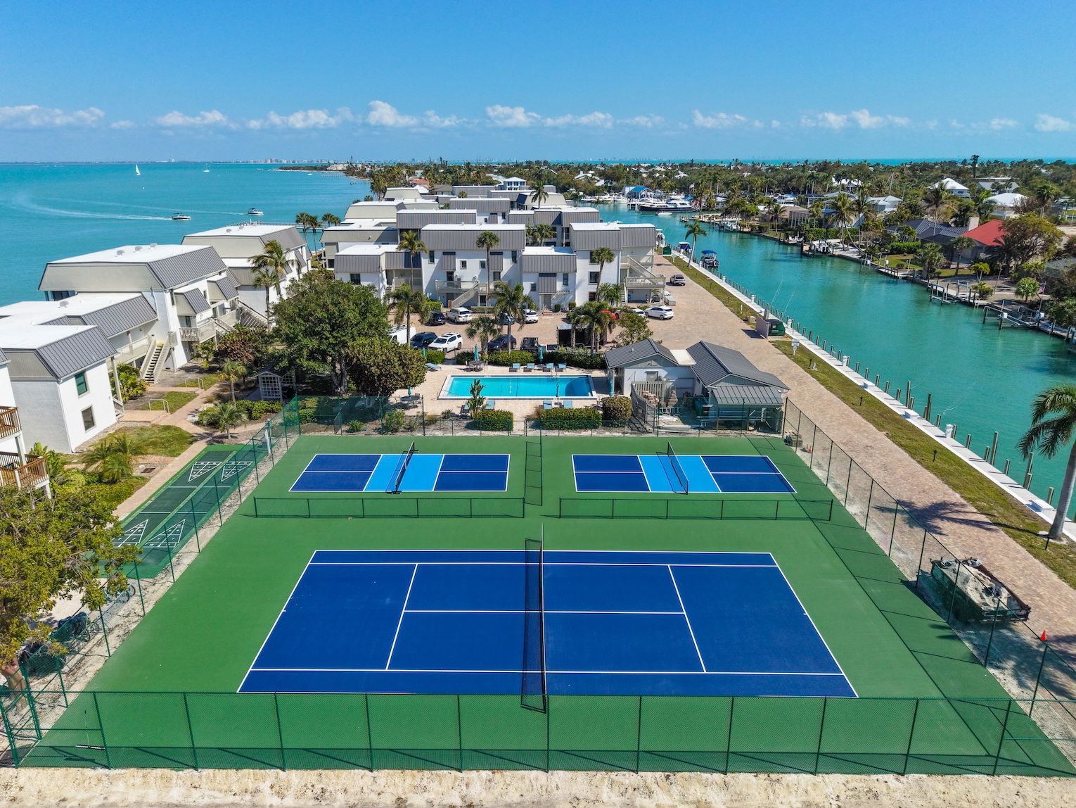 A tennis court with two courts, a pool, and a view of the ocean.