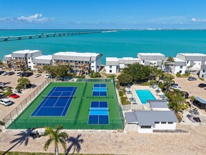 A resort with multiple tennis courts, a pool, and a view of the ocean and a bridge. - Mariner Pointe 951: Updated Bayfront Retreat with Stunning Ground-Level Views (Sanibel)