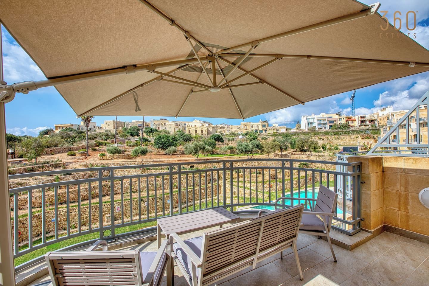 A balcony with a table and chairs, a pool, and a view of buildings in the background.