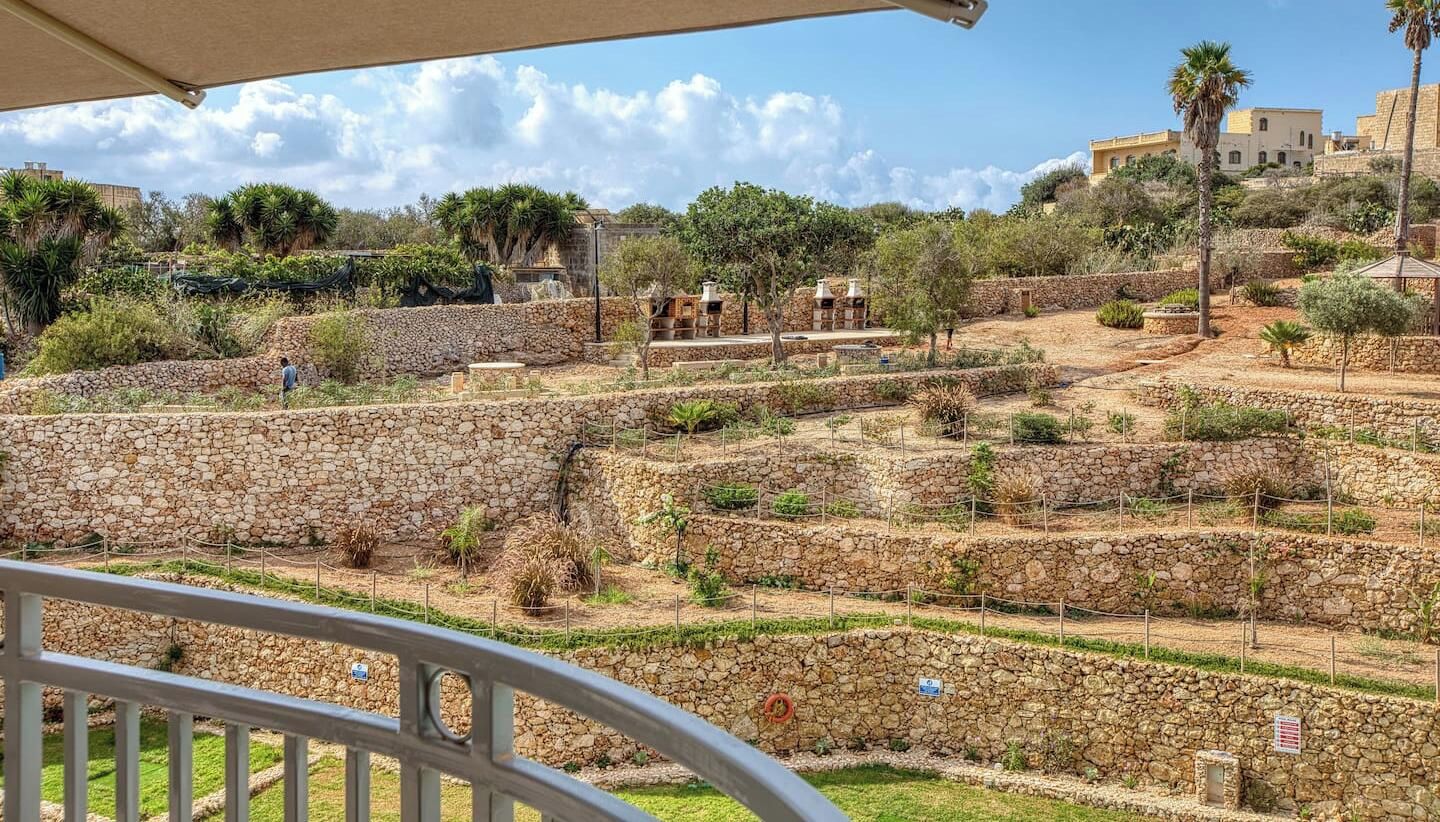 A stone terrace with a view of a hillside, featuring a mix of vegetation and architectural ruins.