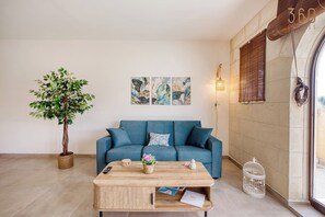A living room with a sofa, coffee table, and a potted plant. - Modern 2BR Qala Gozo Apt with Shared Pools (Qala)