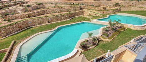 A residential area with two swimming pools, stone walls, and a view of the surrounding neighborhood.