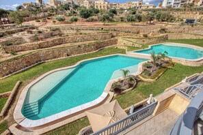 A residential area with two swimming pools, stone walls, and a view of the surrounding neighborhood. - Modern 2BR Qala Gozo Apt with Shared Pools (Qala)