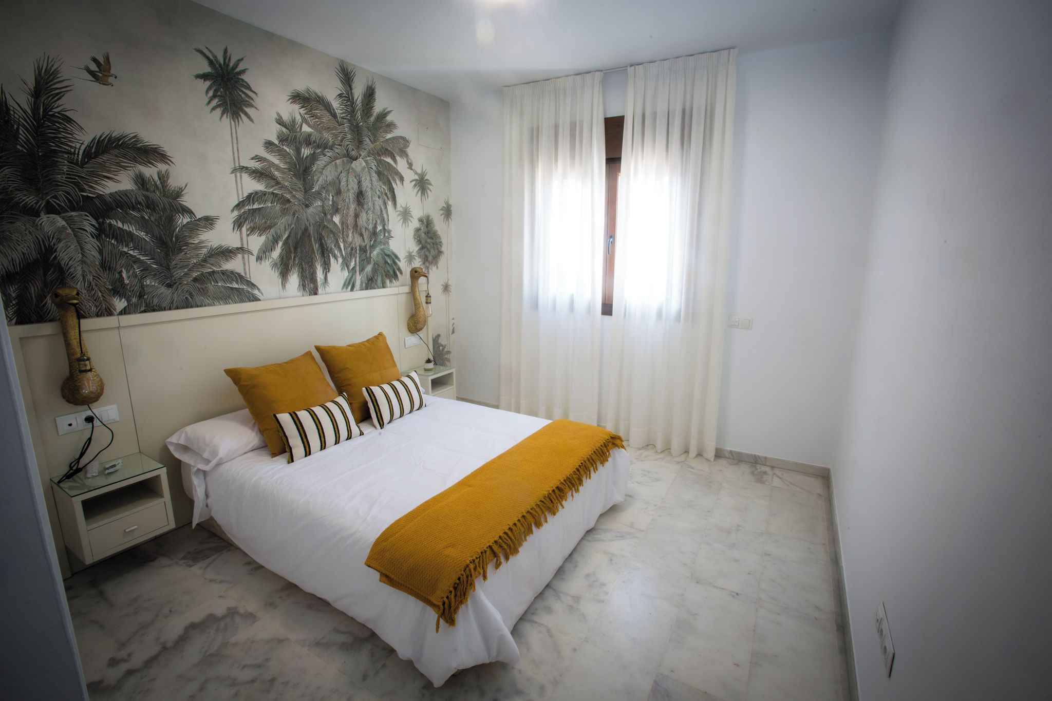 Une chambre à coucher comprenant un lit, une table de chevet, une fresque murale, une fenêtre avec des rideaux et un sol en marbre.