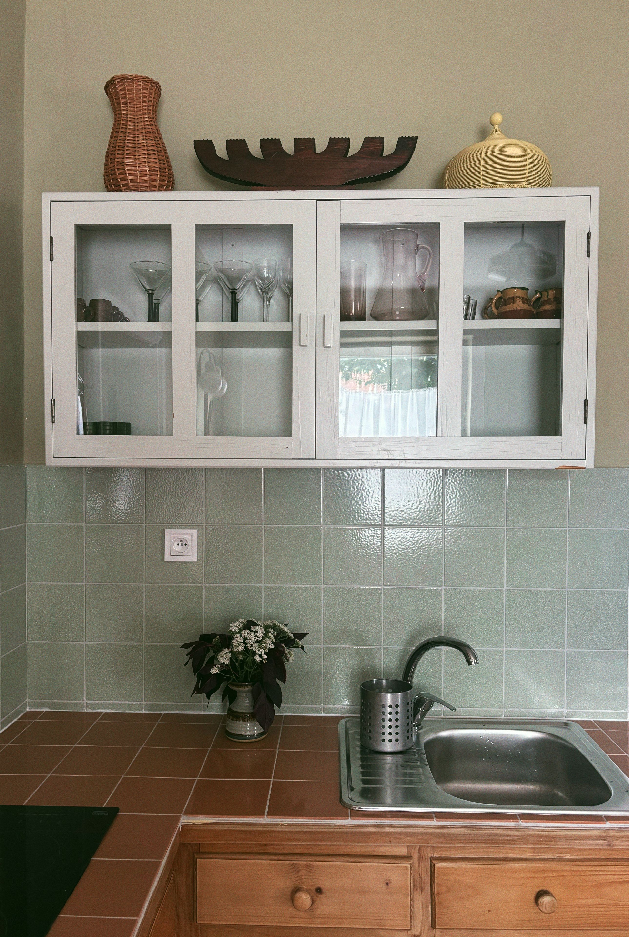 Eine Küche mit weißen Schränken, einem Spülbecken und einer grün gefliesten Rückwand.