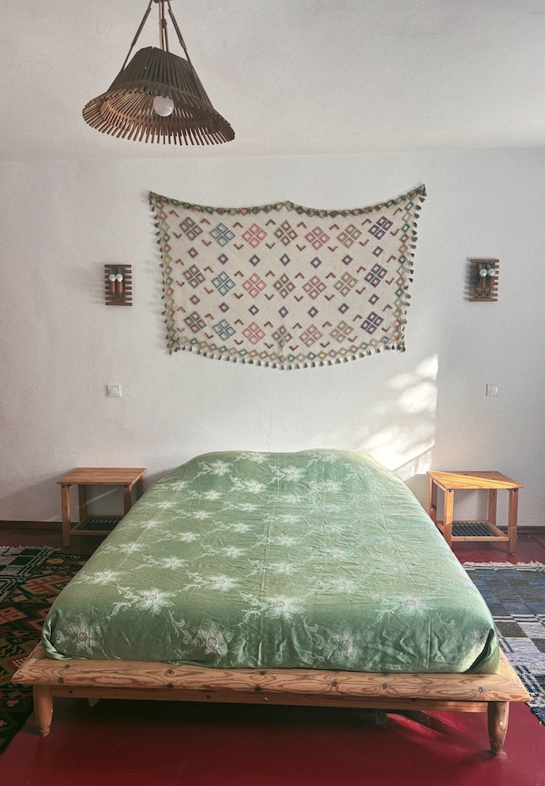 A bedroom with a bed, a hanging light fixture, a tapestry, and a small wooden stool.
