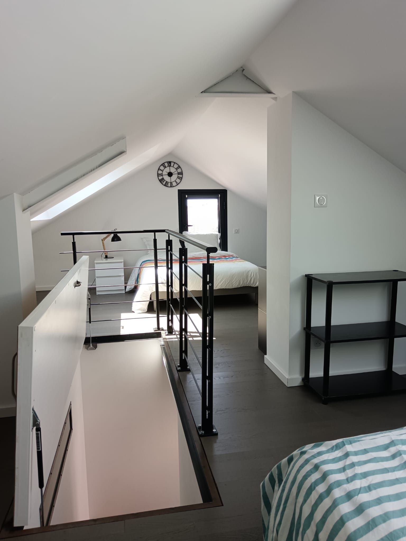 A bedroom with a sloped ceiling, a bed, a bedside table, a lamp, and a clock.
