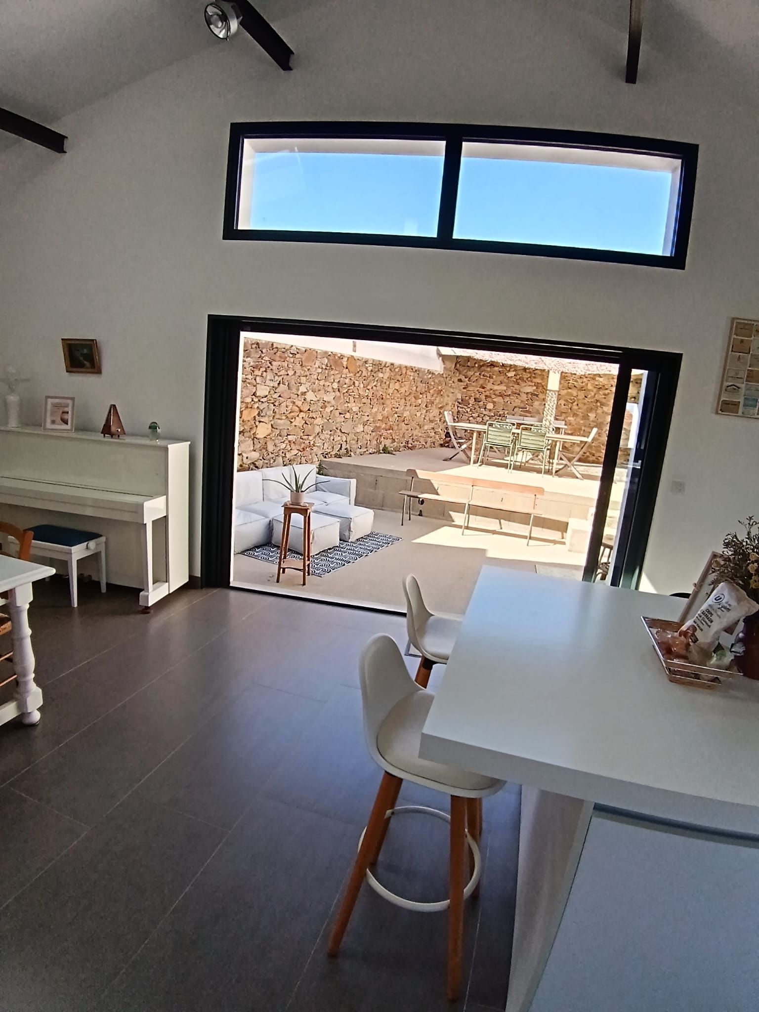 A modern kitchen with a dining area, a large window, and a view of an outdoor patio.