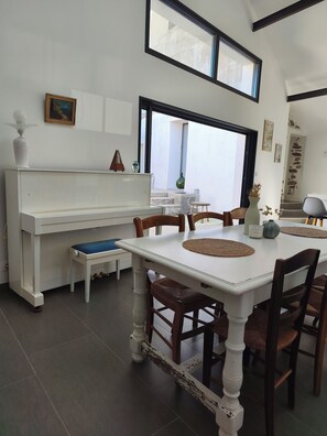 A dining area with a white table, wooden chairs, and a piano. - La Maison de Jeanne - Maison familiale atypique à Brem sur mer (Brem-sur-Mer)