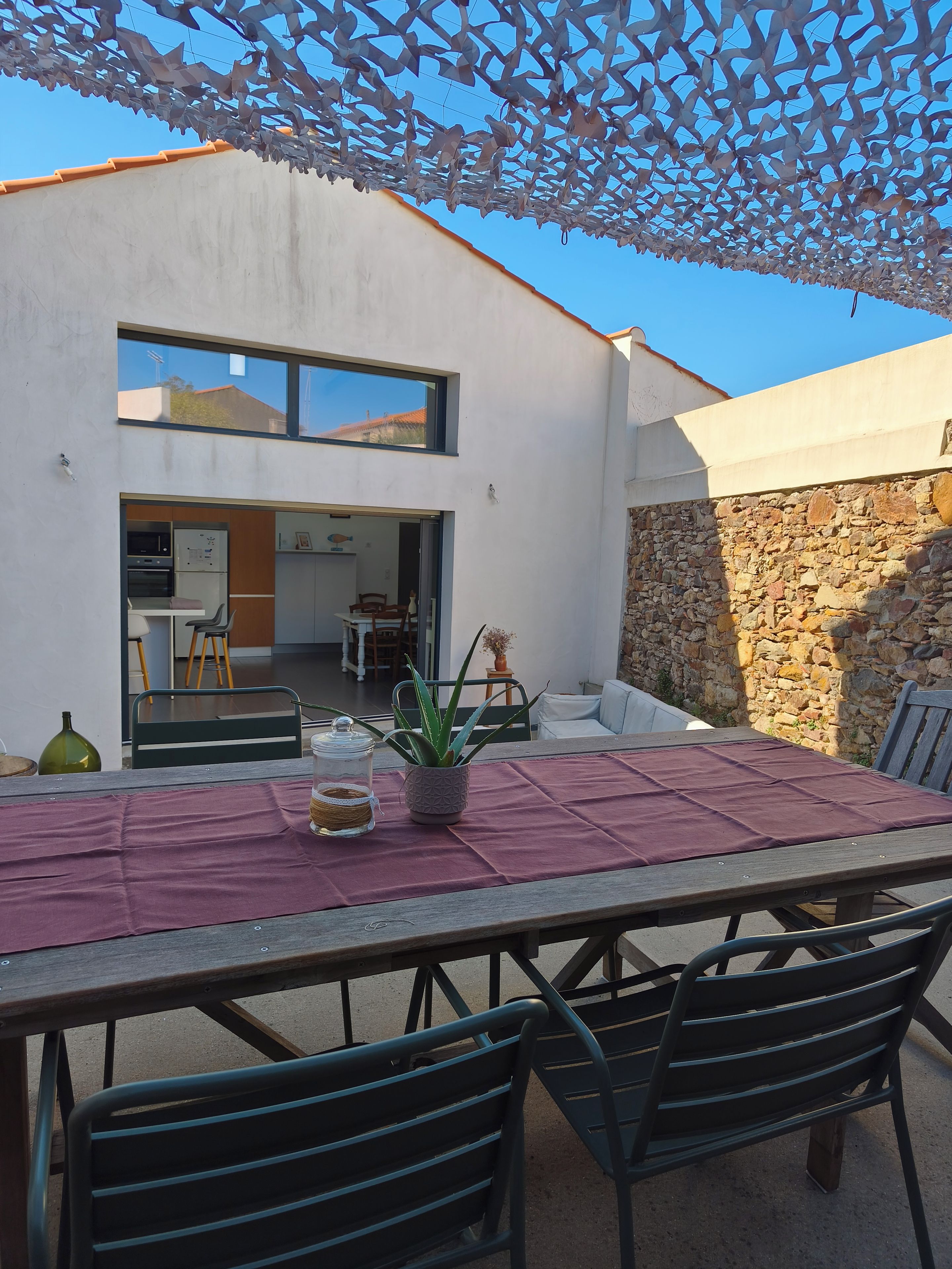 An outdoor patio with a table and chairs, a potted plant, and a stone wall.
