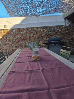 An outdoor dining area with a table covered by a purple cloth, a glass jar with a plant, and a grill in the background. - La Maison de Jeanne - Maison familiale atypique à Brem sur mer (Brem-sur-Mer)