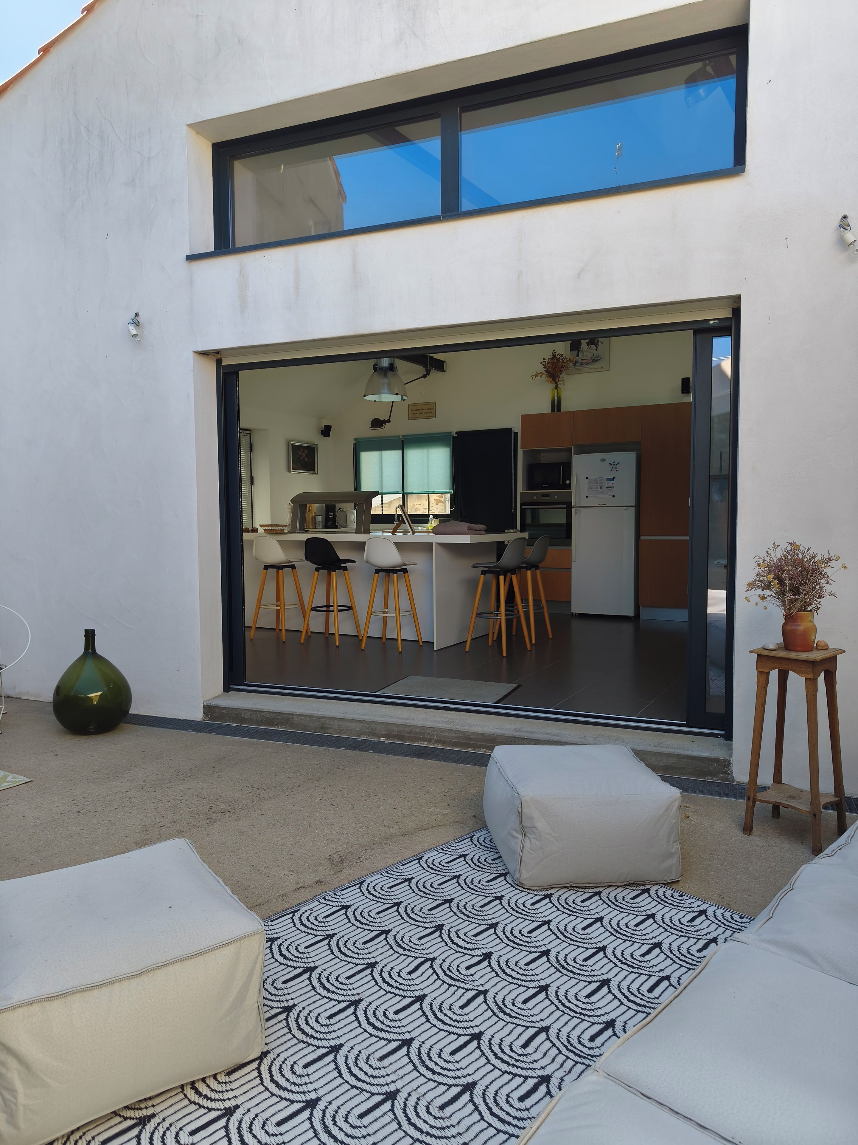 Un espace extérieur moderne, aménagé avec des sièges, un tapis à motifs, un vase vert et un tabouret en bois.