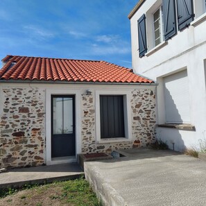 Un edificio de dos pisos con techo de tejas rojas, fachada de piedra y un garaje con persiana cerrada.
