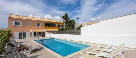 A swimming pool with lounge chairs, a tiled deck, and a building with a tiled roof.