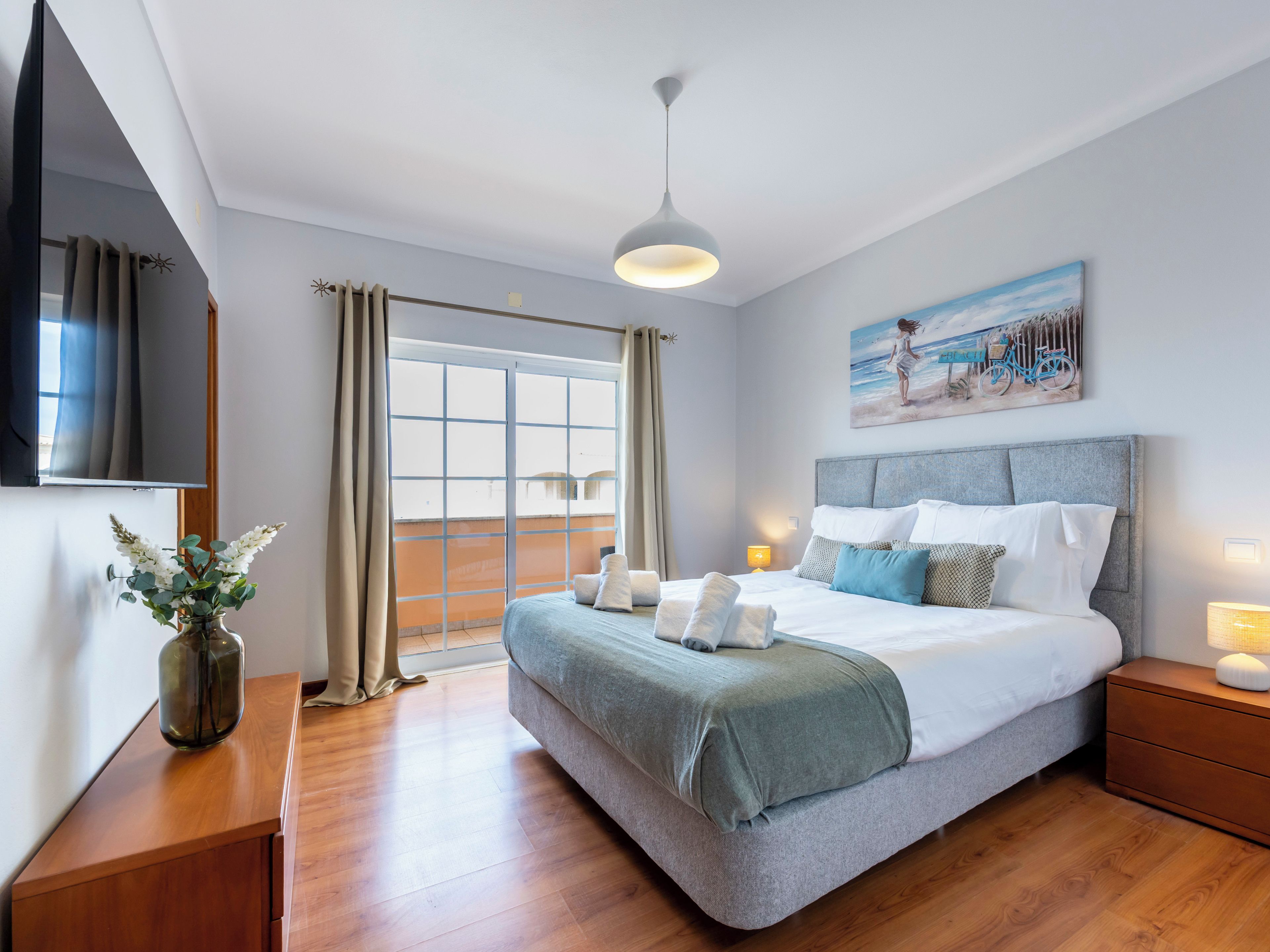 Une chambre d’hôtel moderne avec un grand lit, un téléviseur à écran plat, un tableau et une table de chevet en bois.