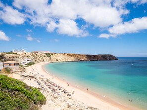 A coastal beach with a sandy shore, clear turquoise waters, and a rocky cliff. - The Sagres House - Village Pool Retreat (Sagres)
