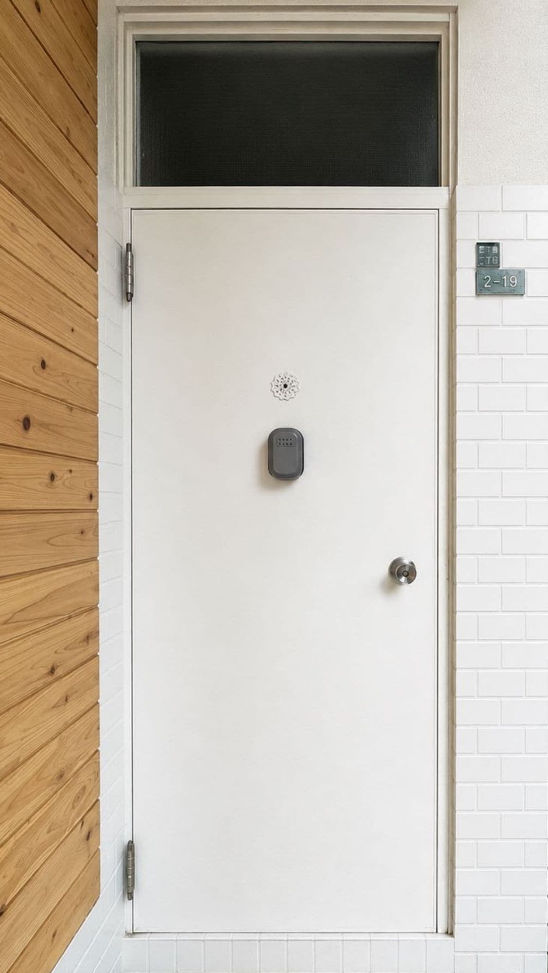 Una puerta blanca con cerradura electrónica, un felpudo y un buzón en la pared.