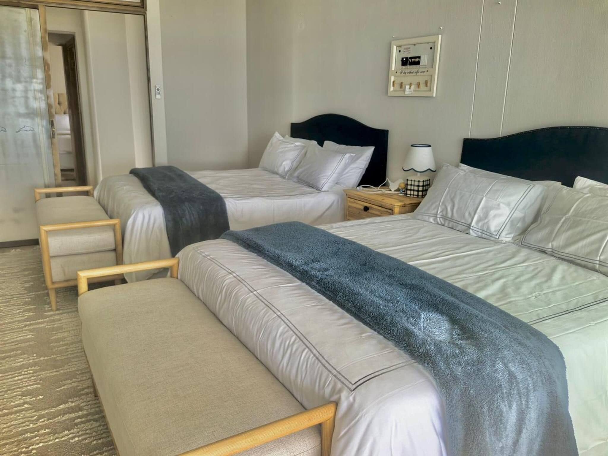 A hotel room with two beds, a bench, a nightstand, and a wall-mounted light fixture.