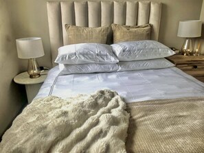 A neatly made bed with a fluffy white throw blanket, a headboard with vertical panels, and bedside lamps on wooden nightstands. - 10 C-front Penthouse (Margate)