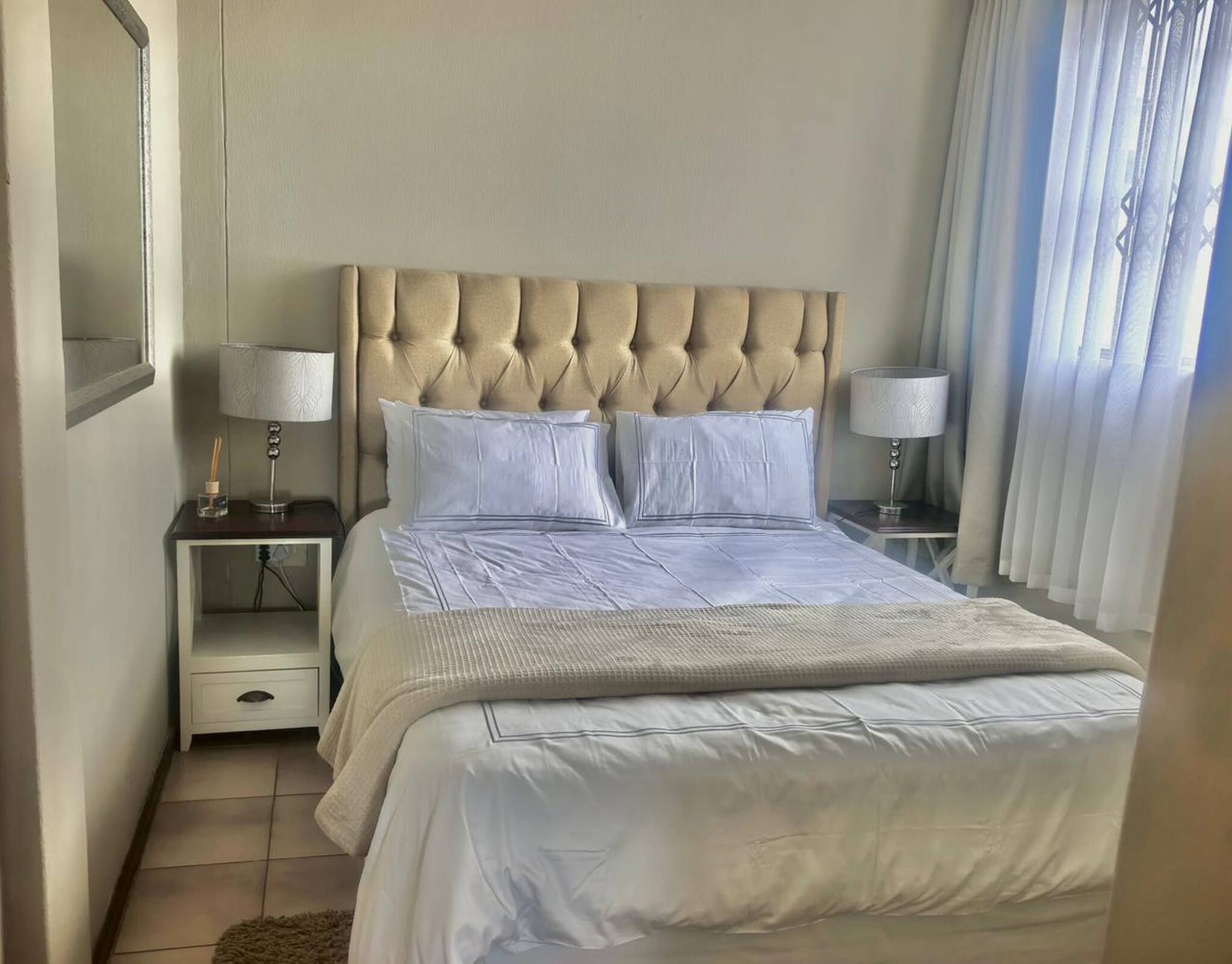A hotel room with a large bed, two bedside tables, a nightstand, a mirror, and a window with curtains.