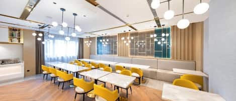 A modern dining area with multiple tables and chairs, a long bench, and a large window providing natural light.