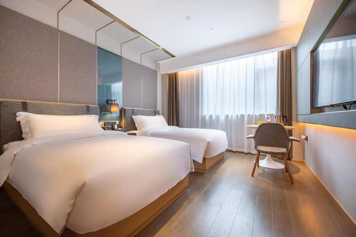 A hotel room with two beds, a desk, a chair, and a TV.