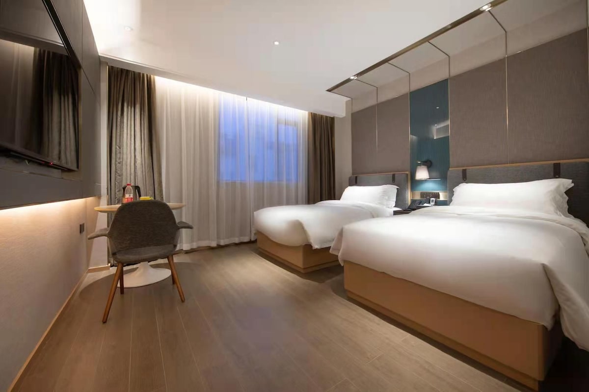 A hotel room with two beds, a desk, a chair, and a TV.