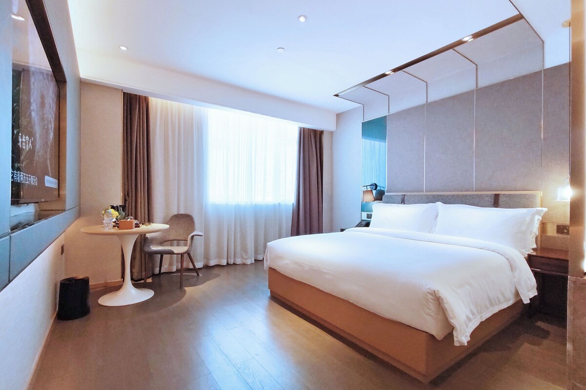 A hotel room with a large bed, a desk, a chair, and a window with curtains.