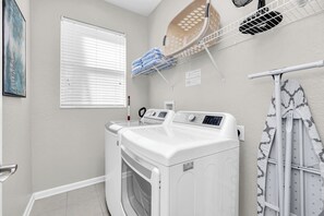 A laundry area with a front-loading washer and dryer, a drying rack, and a window with blinds. - 6BD Mins to Disney | Pool, Spa, Theater, Game Room (Kissimmee)