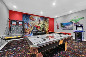 A room with a foosball table, a ping pong table, and a large mural of superheroes. - 6BD Mins to Disney | Pool, Spa, Theater, Game Room (Kissimmee)
