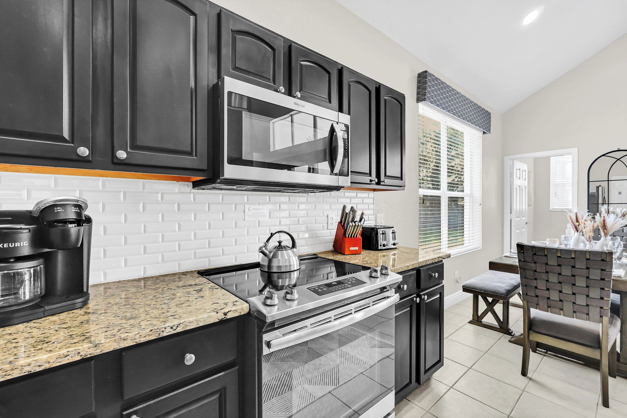 A modern kitchen with black cabinets, a stainless steel range, a microwave, and a kettle.