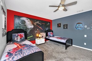 Un dormitorio con dos camas, ventilador de techo y decoración temática de Star Wars.