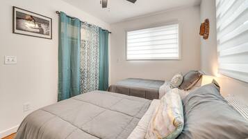 Un dormitorio con dos camas, un ventilador de techo, una ventana con persianas y un cuadro enmarcado en la pared.