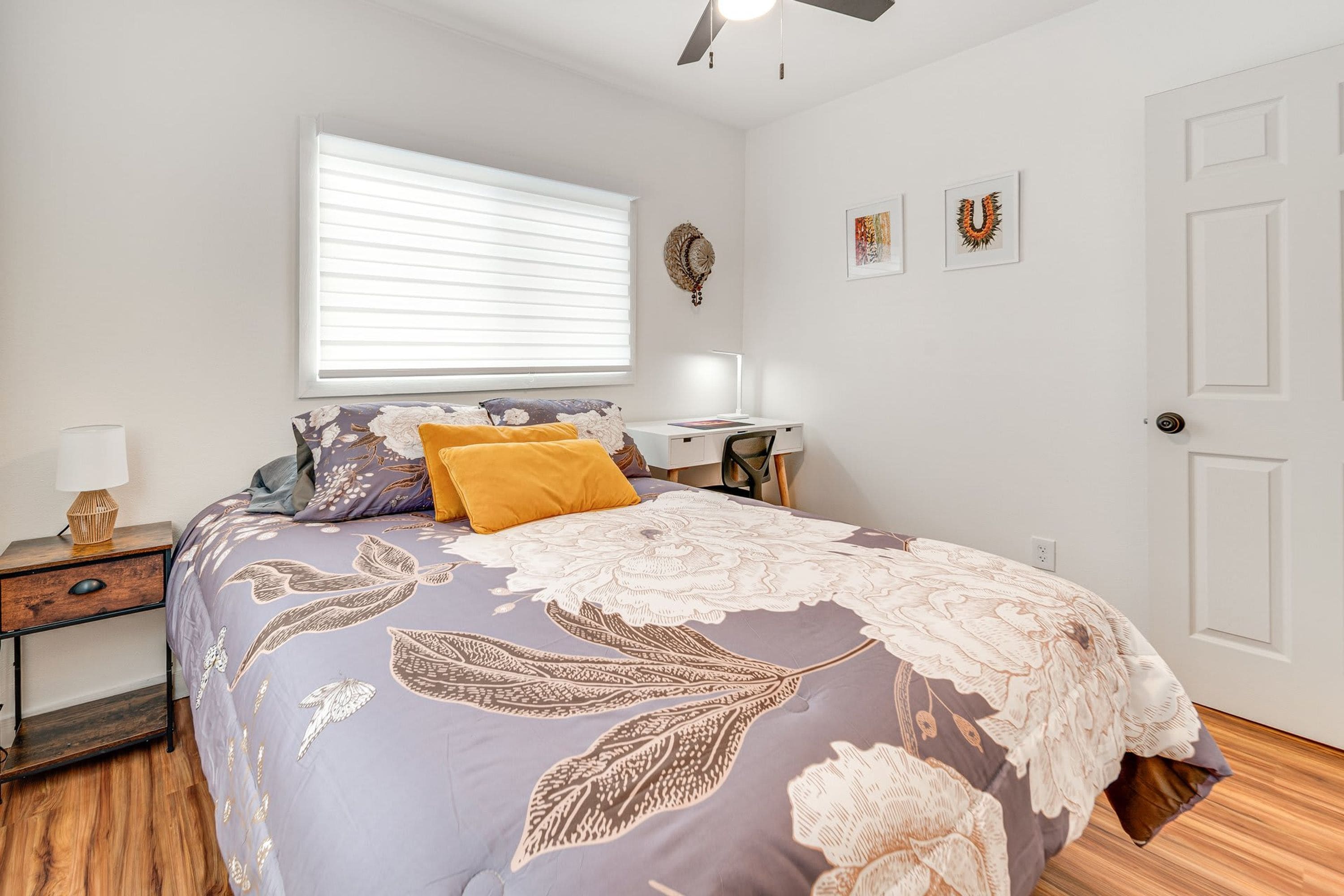 A bedroom with a bed, bedside table, lamp, wall art, and a door.