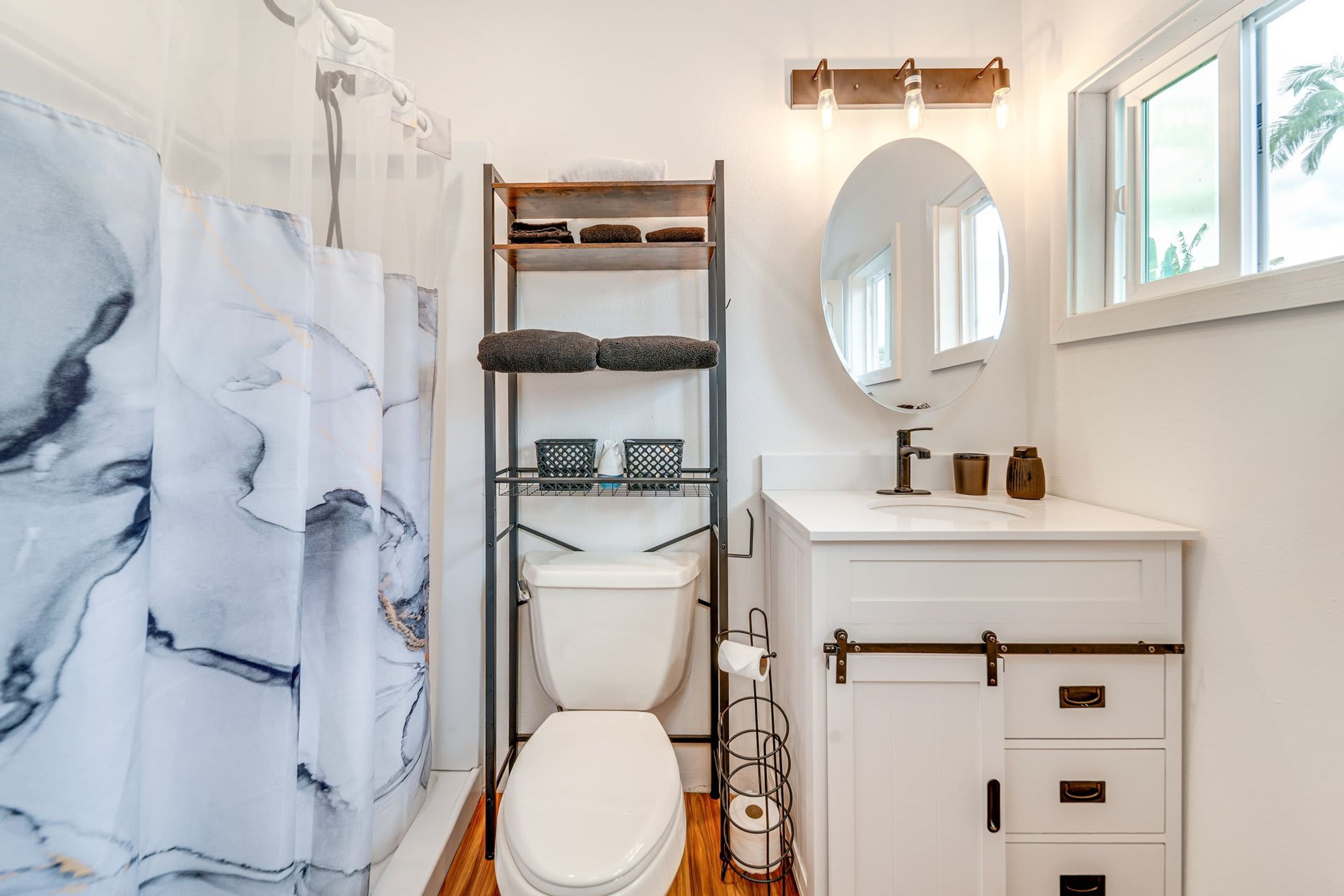 A bathroom with a toilet, a shelf with towels, a mirror, and a window.