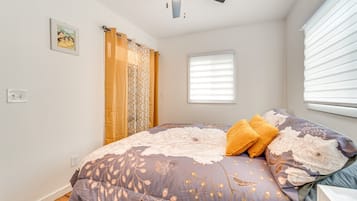 Ein Schlafzimmer mit einem Bett, einem Deckenventilator, einem Fenster mit Jalousien und einem an der Wand befestigten Lichtschalter.